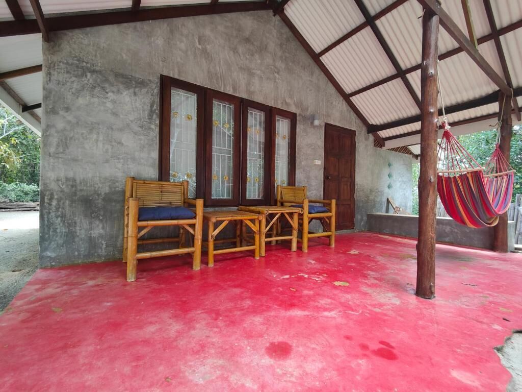 A covered outdoor seating area with wooden chairs and a table, a red floor, and a hanging hammock.
