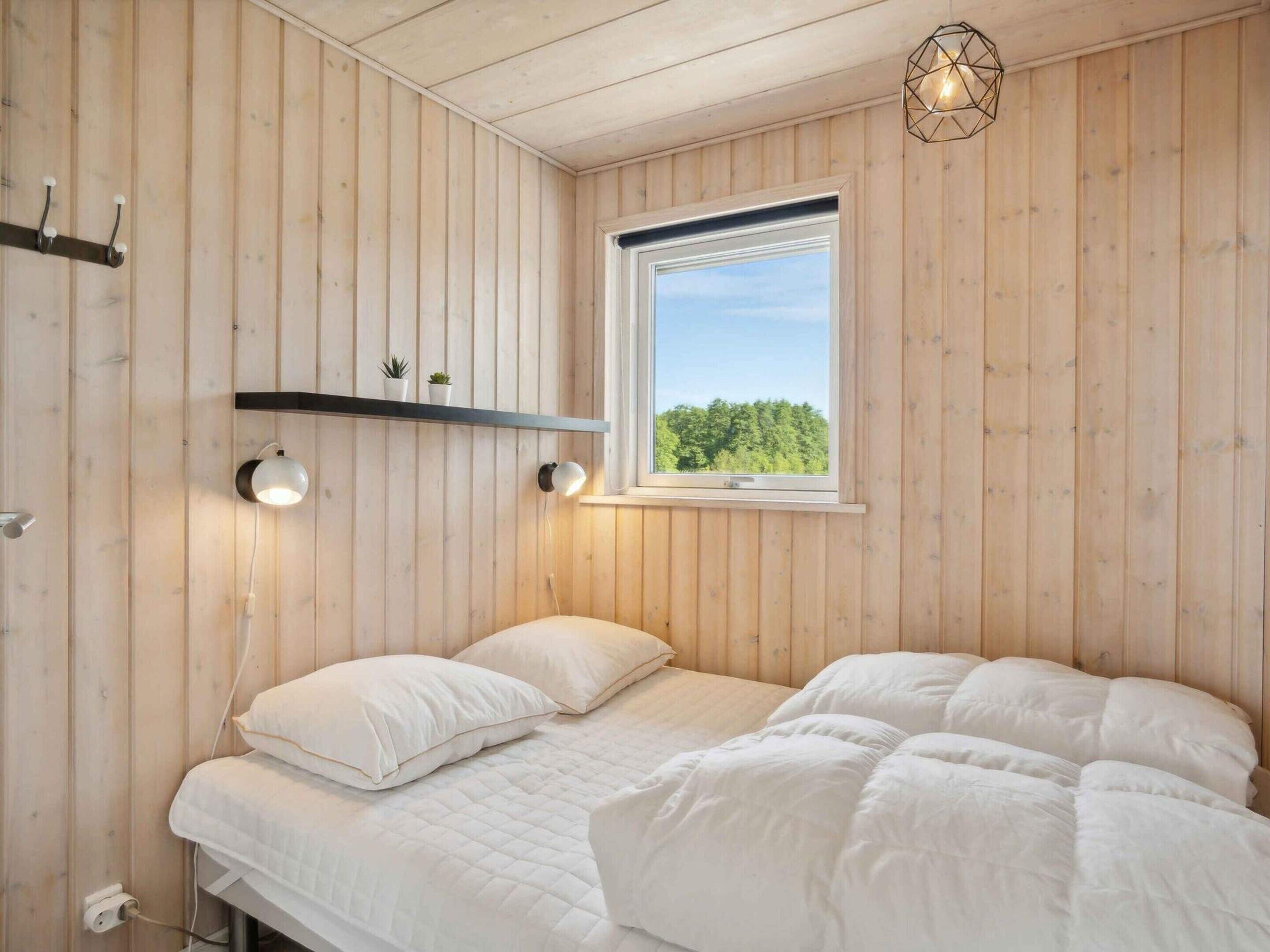 Een slaapkamer met houten wanden, een bed met witte beddengoed, een raam met uitzicht op bomen, en een wandplank met planten.