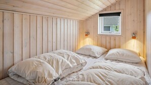 A cozy wooden cabin room with a bed, two wall-mounted lamps, and a window.