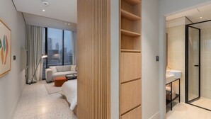 Camera d'albergo moderna con vista sulla città, un divano, un pannello in legno e un bagno con doccia in vetro.