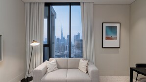 Un soggiorno moderno con un divano, una lampada da terra, un quadro incorniciato e vista su un orizzonte cittadino attraverso ampie finestre.