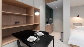Una camera d'albergo moderna con un tavolo da pranzo per quattro persone, un angolo cottura e un letto con biancheria da letto bianca.
