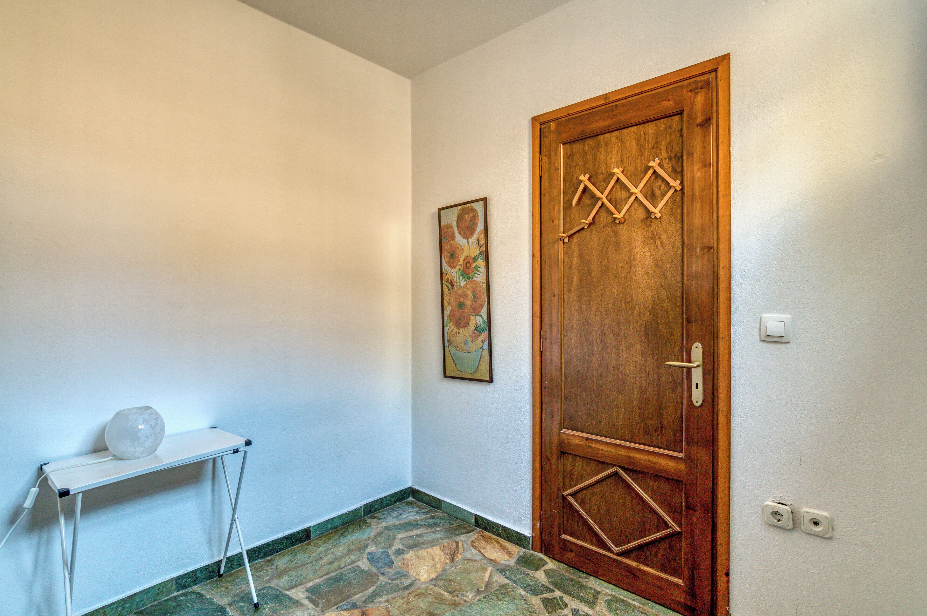A hallway with a wooden door, a small table with a vase, and a painting on the wall.