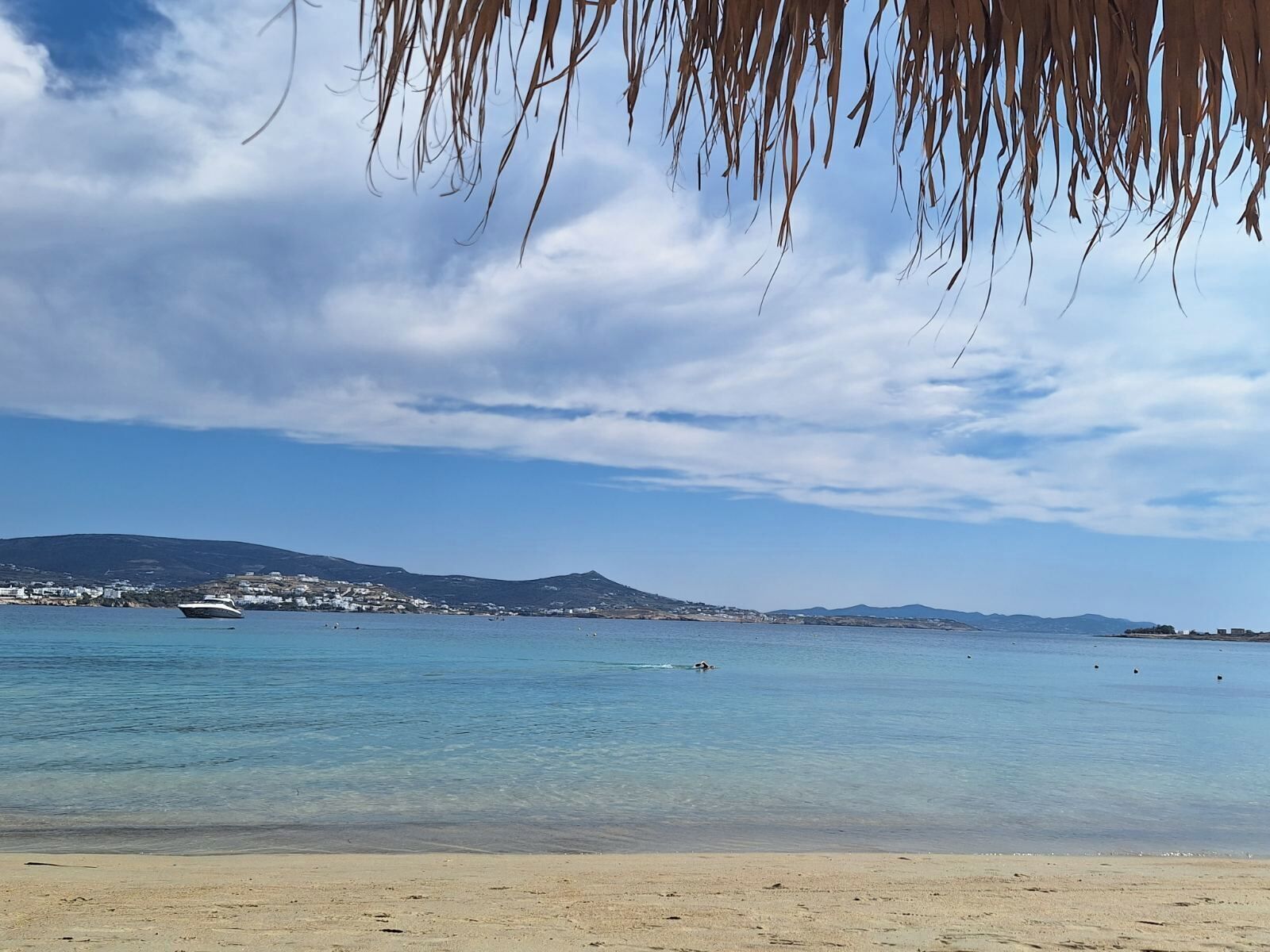 A beach with clear water, a boat, and distant hills.