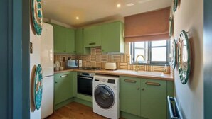 A compact kitchen with green cabinets, a washing machine, and a microwave.