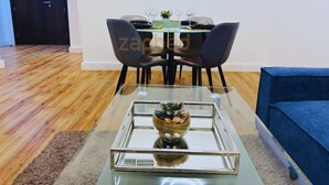A modern dining area with a glass table, four chairs, and a blue sofa. - RAK F 211 (Ras Al Khaimah)