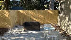 A patio with a wooden fence, a wicker sofa, and a metal table with chairs.