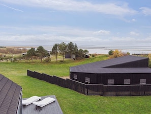 A view of a property with a grassy yard, a wooden fence, and a building with a dark roof.