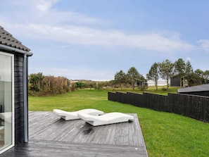 A deck with two white lounge chairs and a wooden deck.