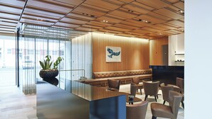 A modern reception area with a wooden ceiling, a large bench, and several chairs. - Hotel am See (Hard)