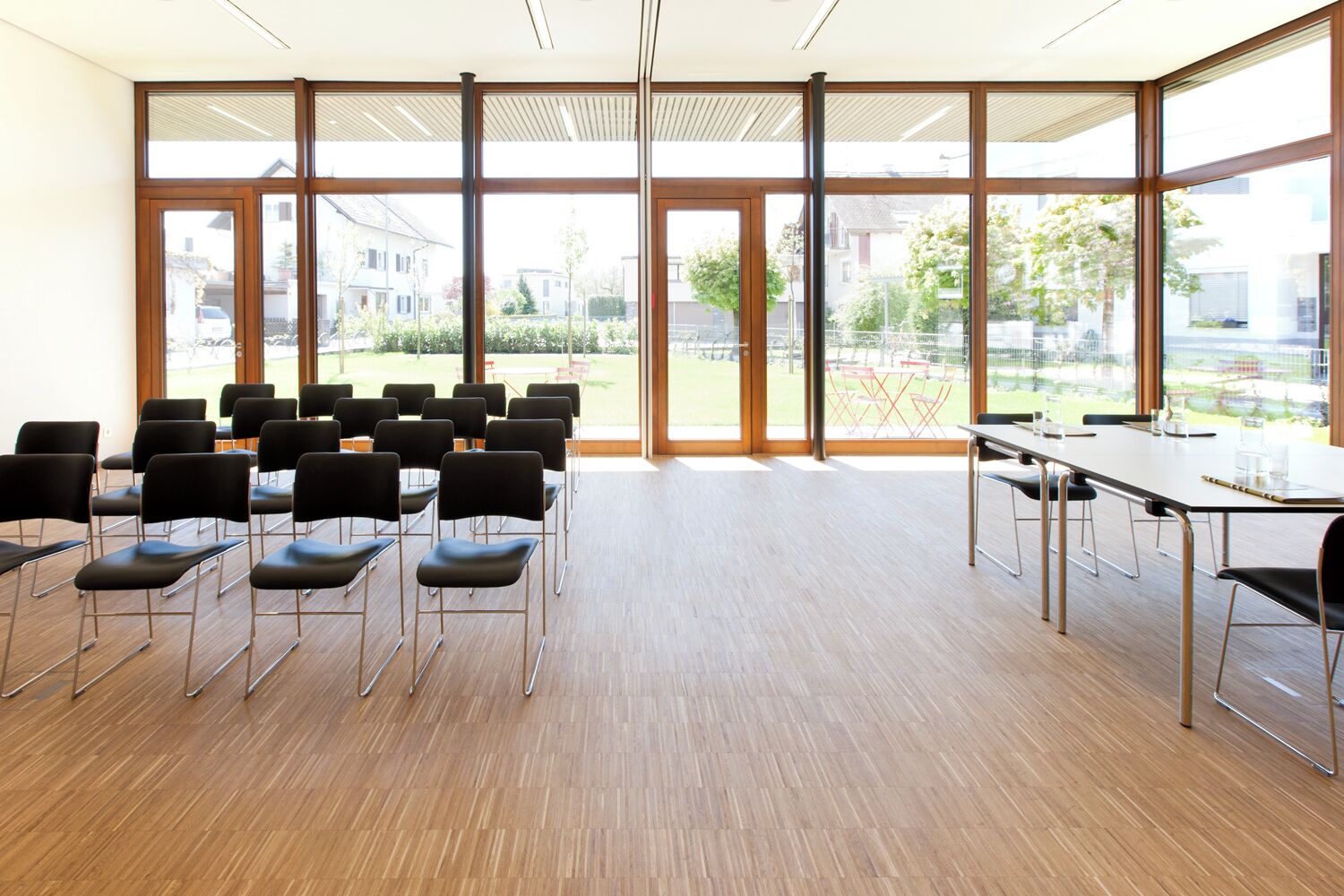 A conference room with a large table and chairs, large windows with a view of a residential area.