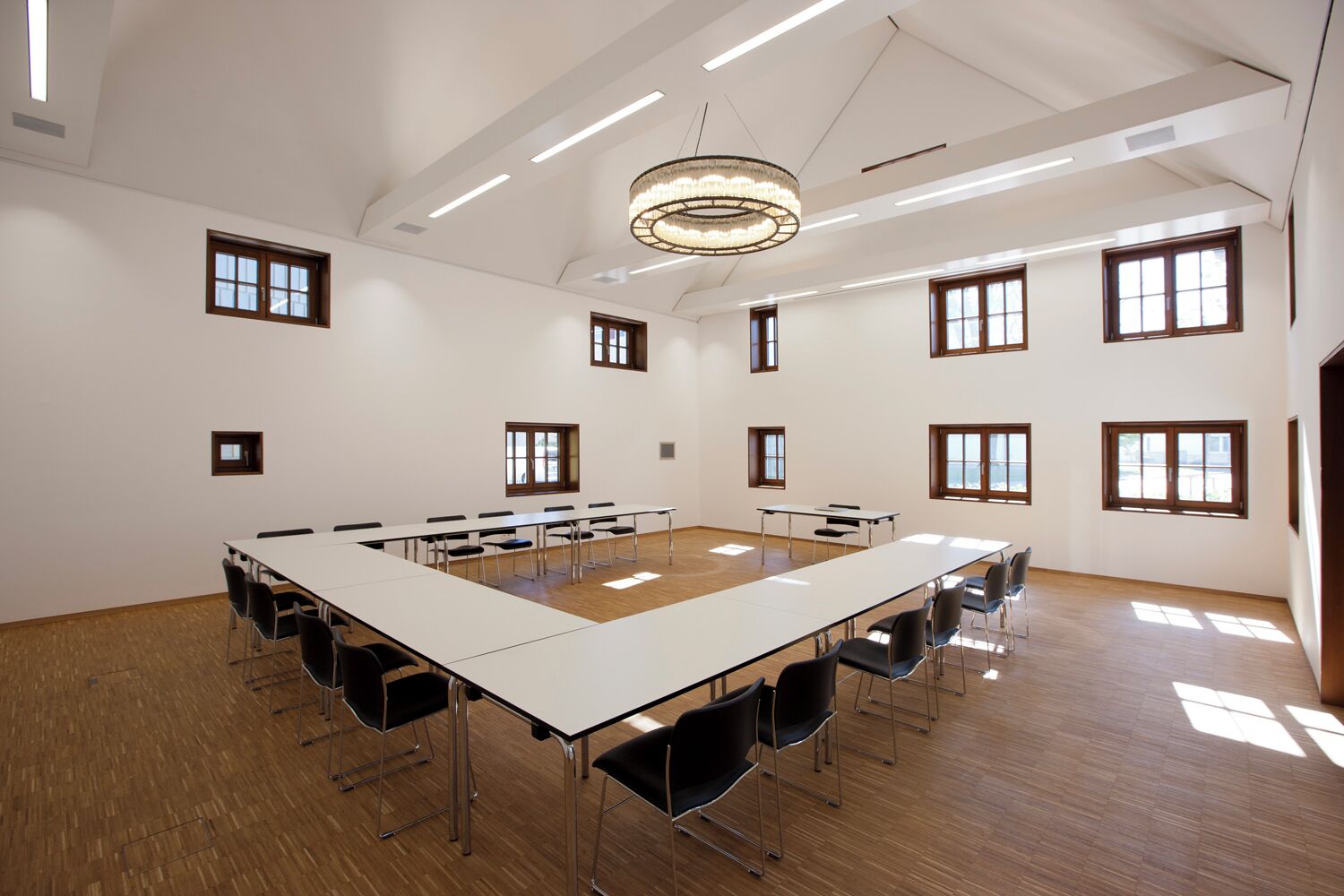 Una amplia sala de conferencias con una larga mesa, múltiples sillas y grandes ventanales que dejan entrar luz natural.