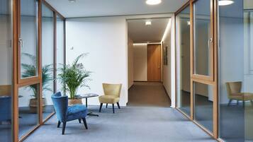 A hallway with glass doors, a blue chair, a yellow chair, and a small table with a plant.