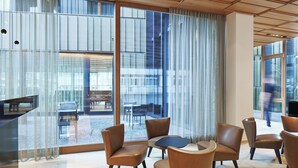 A modern interior with leather chairs and a small round table, large windows with curtains, and a view of outdoor seating. - Hotel am See (Hard)