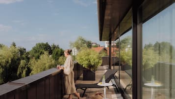 Ein Balkon mit einer Person, die am Geländer steht, einem Tisch, einem Stuhl und einem Getränk.