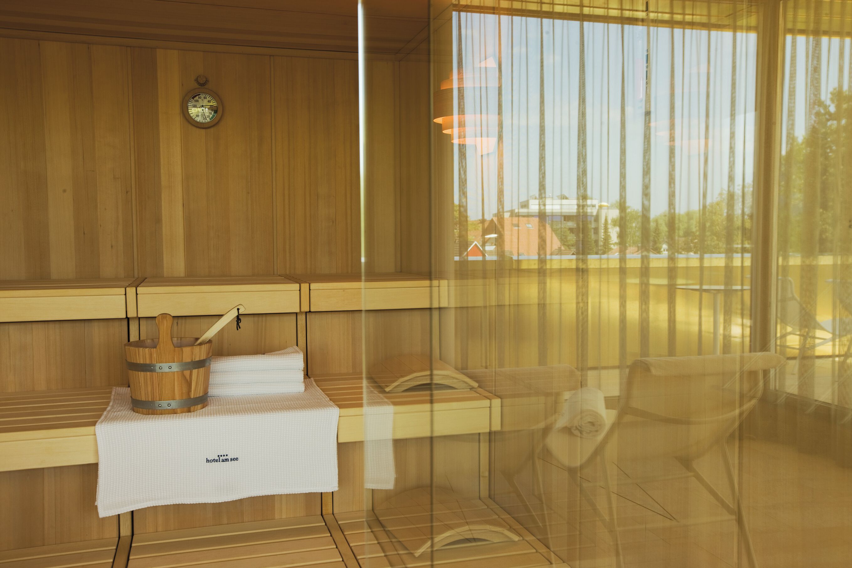A sauna room with wooden walls, a wooden bucket, a towel, and a clock on the wall.