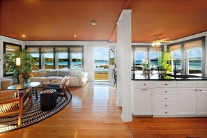 A spacious living area with a view of the beach, a kitchen with white cabinets, and a dining area with a table and chairs.