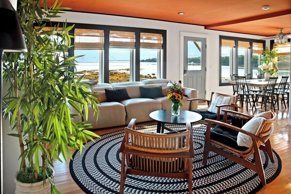 A living room with a sofa, chairs, a coffee table, and a view of the beach.