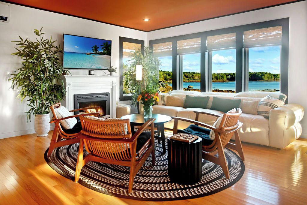 A modern living room with a fireplace, a television, and a view of a beach.
