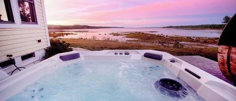 Un bain à remous extérieur avec vue sur un plan d’eau et un coucher de soleil.