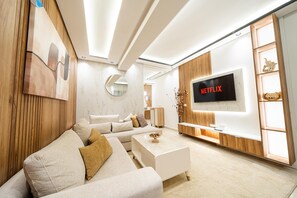 Un salon moderne avec un canapé blanc, une table basse et un téléviseur fixé au mur, qui affiche le logo de Netflix.