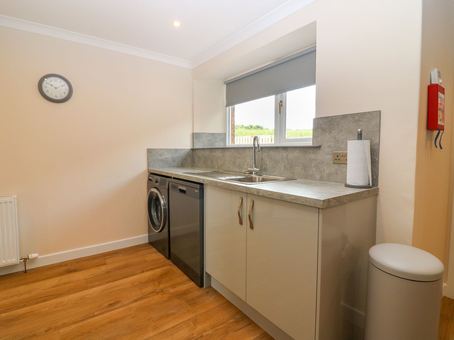 A compact kitchen with a washing machine, a sink, and a trash bin.