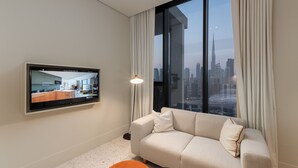 A modern living room with a large window, a flat-screen TV, a sofa, and a small orange table. - Burj View Studio Near Downtown and Canal (Dubai)