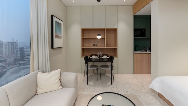 A modern hotel room with a dining area, kitchenette, and a large window with a city view. - Burj View Studio Near Downtown and Canal (Dubai)