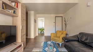 A modern living room with a sofa, armchair, TV, and wooden shelving unit. - Appartamento Pacini by Wonderful Italy (Palermo)