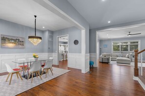 A modern living room with a wooden floor, a glass dining table with chairs, a sofa, and a ceiling fan. - Stunning 6-bedroom house in Falls Church-Luxury Awaits! (Falls Church)