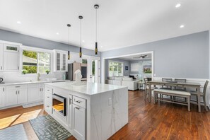 A modern kitchen with white cabinetry, a marble island, and a dining area with a wooden table and bench. - Stunning 6-bedroom house in Falls Church-Luxury Awaits! (Falls Church)