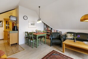 A compact living space with a dining area, a sofa, a coffee table, a bookshelf, and a kitchen area.