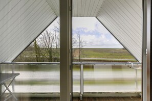 A room with a large window, a table, and a view of a landscape with trees and a field.