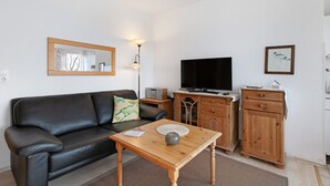 A living room with a black leather sofa, a wooden coffee table, a television, and a cabinet. - Apartment 'Fewo 3 Gröde' with Shared Terrace, Shared Garden and Wi-Fi (Dagebüll)