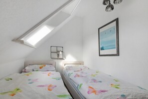 A bedroom with two beds, a skylight, a framed picture, and a bedside table.