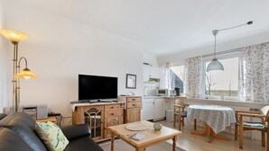 A living room with a sofa, a coffee table, a TV, a kitchen area, and a dining table with chairs. - Apartment 'Fewo 3 Gröde' with Shared Terrace, Shared Garden and Wi-Fi (Dagebüll)