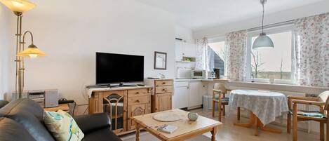Una sala de estar con sofá, mesa de centro, televisor, zona de cocina y mesa de comedor con sillas.