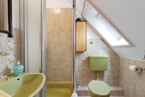 A bathroom with a green sink, a shower, a toilet, and a skylight.