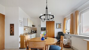 A dining area with a round table, chairs, a chandelier, and a window with curtains. - Apartment 'Fewo 5 Hamburger Hallig' with Shared Terrace, Shared Garden and Wi-Fi (Dagebüll)