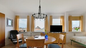 A room with a dining table, chairs, a TV, a bed, and windows with curtains. - Apartment 'Fewo 5 Hamburger Hallig' with Shared Terrace, Shared Garden and Wi-Fi (Dagebüll)
