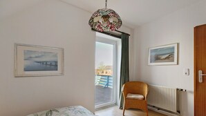 Ein Zimmer mit einem Bett, einem Korbstuhl, einem Heizkörper und zwei gerahmten Bildern an der Wand.