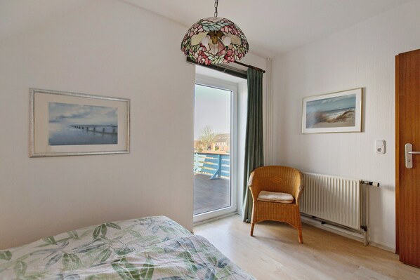 A room with a bed, a wicker chair, a radiator, and two framed pictures on the wall.