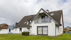 Ein weißes, zweistöckiges Haus mit Satteldach, einem sichtbaren Dachfenster und einer großen Schiebeglastür.