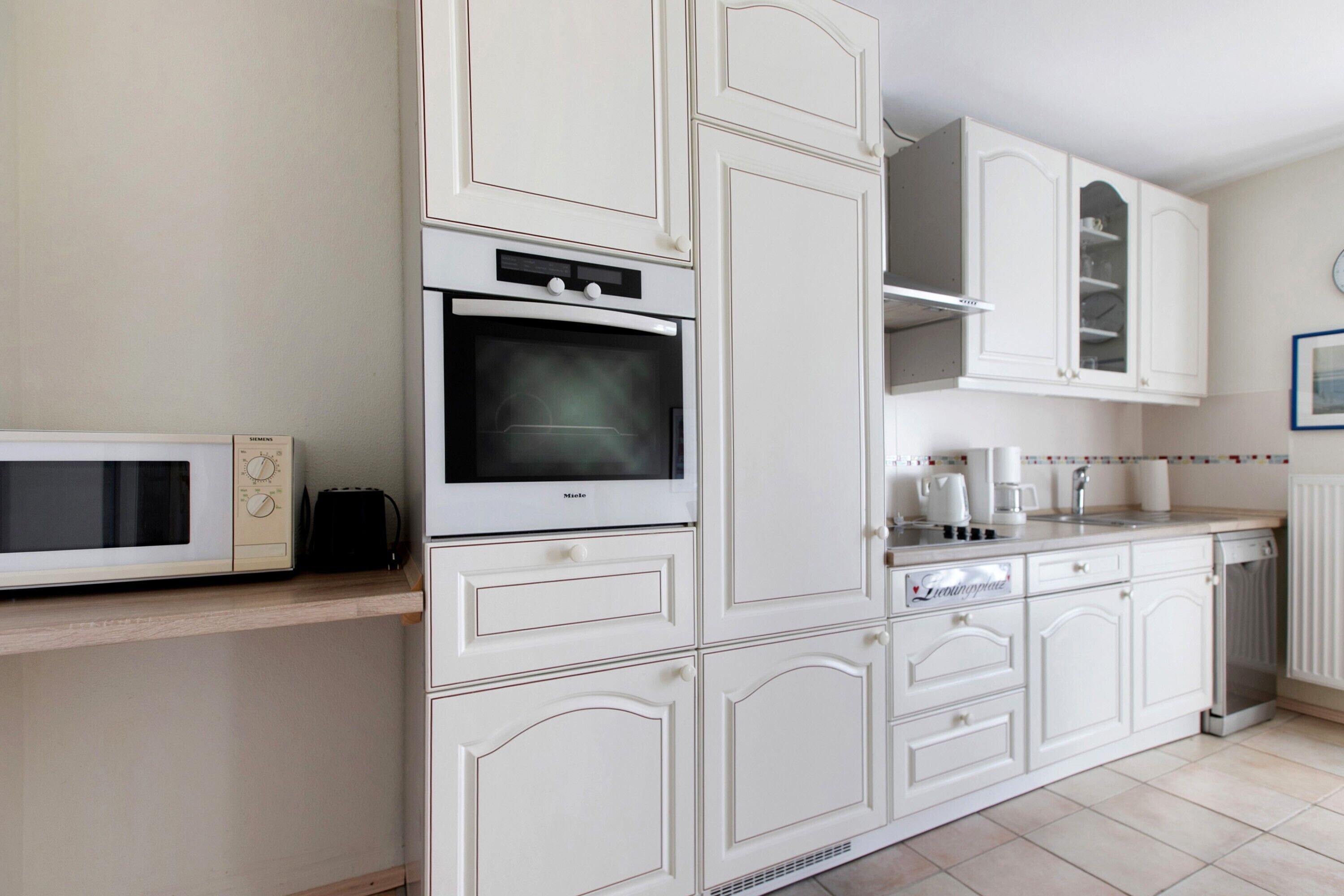 A kitchen with white cabinets, a microwave, an oven, a sink, and a dishwasher.