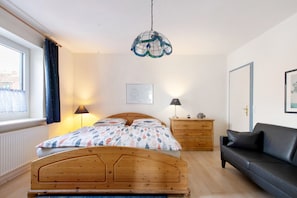 Une chambre à coucher avec un lit en bois, un canapé noir, une table de chevet avec une lampe, un luminaire suspendu et une fenêtre avec des rideaux.