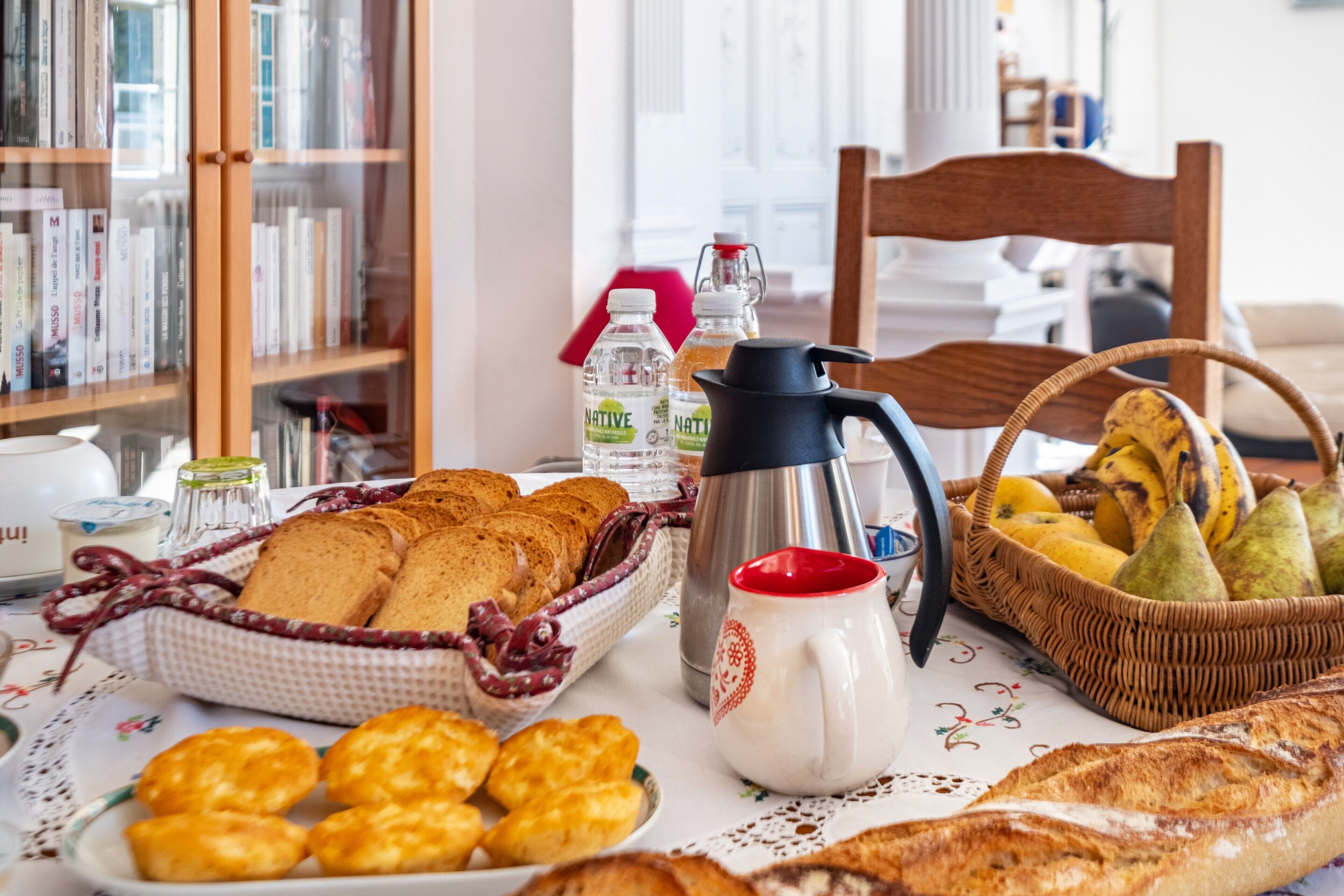 Een ontbijttafel met brood, gebak, een koffiepot en flessen.