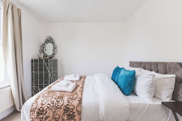 A hotel room with a bed, a dresser, a mirror, and a window with curtains.