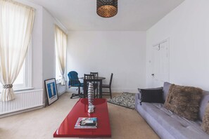 A living room with a red coffee table, a sofa, a dining table with chairs, and a chandelier.