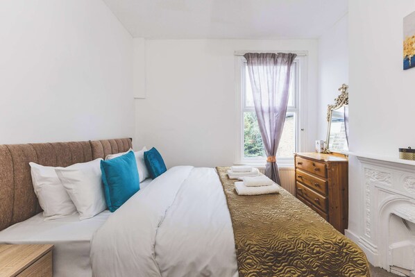 A bedroom with a bed, a dresser, a mirror, and a fireplace.