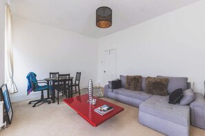 A living room with a red coffee table, a grey sofa, and a dining area with chairs and a table.